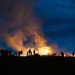 Eine Gruppe von Menschen steht nachts um ein Lagerfeuer.