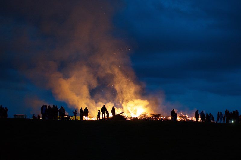 Eine Gruppe von Menschen steht nachts um ein Lagerfeuer.